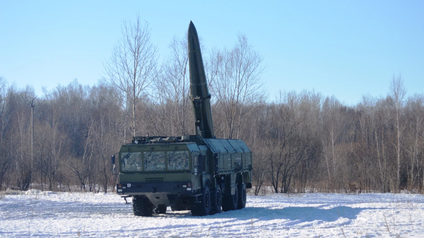 Mobilna wyrzustnia systemu Iskander wraz z załadowanym pociskiem Wojskowa mobilna wyrzutnia rakiet balistycznych ustawiona na śnieżnym polu, w tle widoczne bezlistne drzewa.