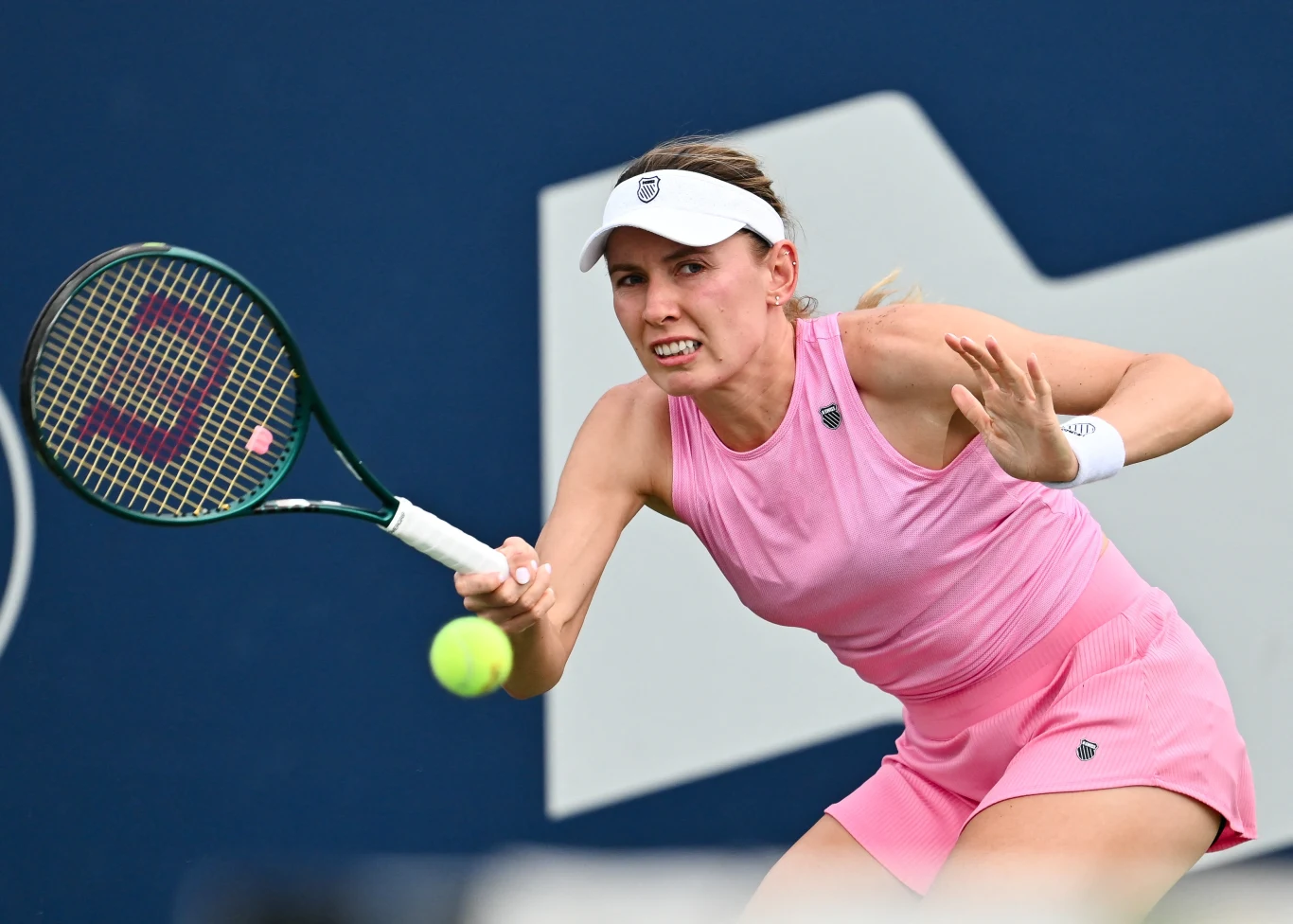 Tenista vestido de rosa durante un juego intenso, centrado en golpear la pelota de tenis, al fondo una cancha azul con elementos gráficos blancos