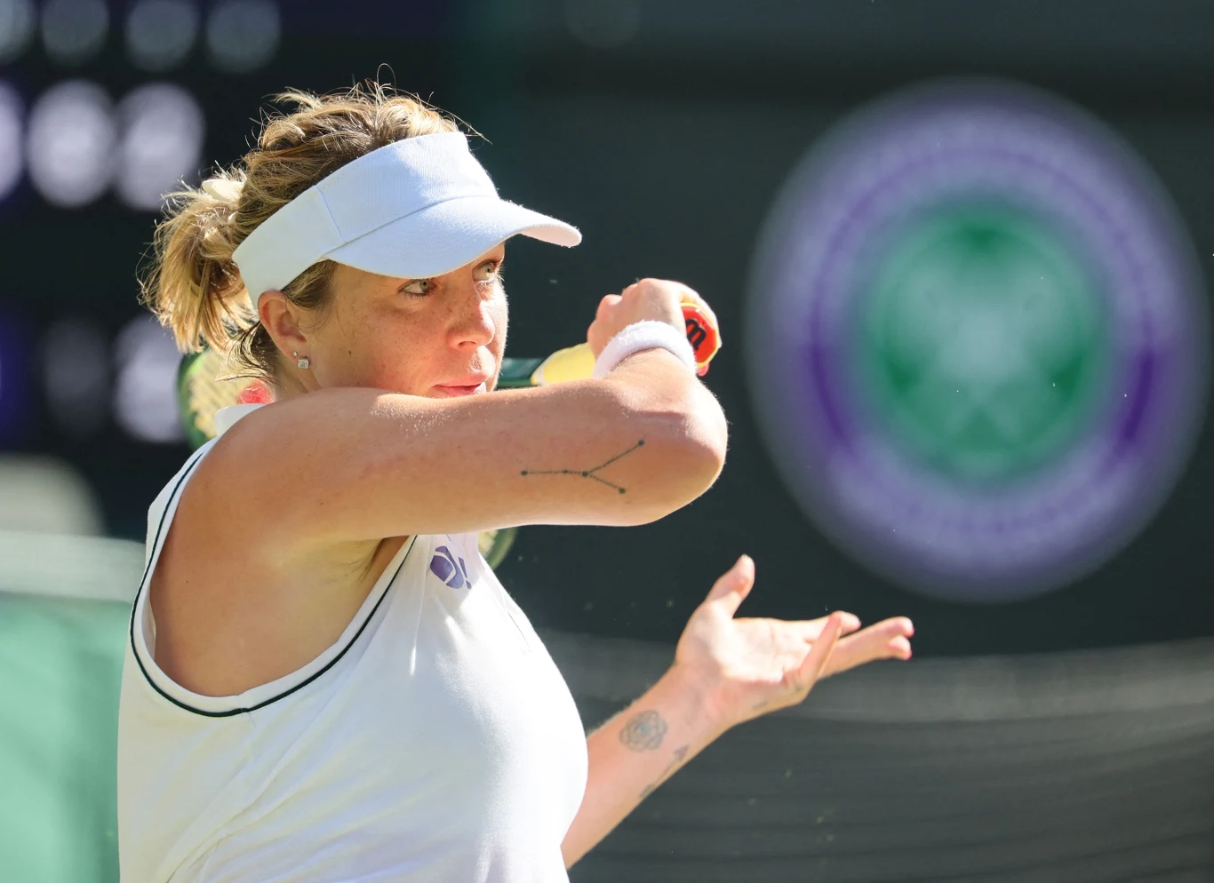 Anastazja Pawluczenkowa Kobieta w białym stroju sportowym i czapce z daszkiem podczas gry w tenisa na tle kortu z wyraźnym logo turnieju Wimbledon.