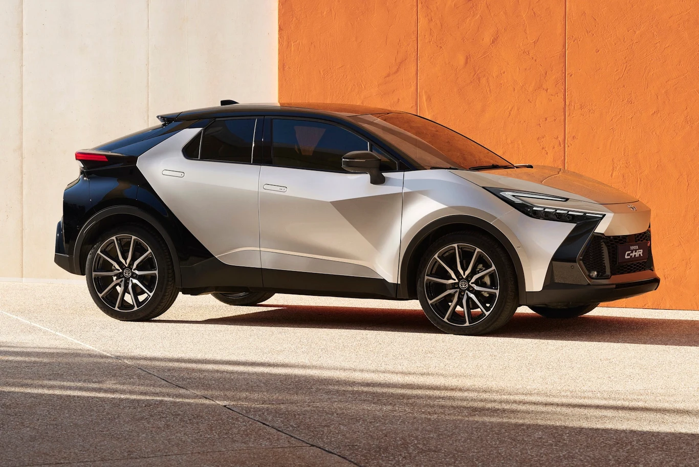 Nowoczesny samochód osobowy typu crossover o dynamicznym, futurystycznym designie, nadwoziu w dwóch kontrastujących kolorach, stojący na tarasie z jasną i pomarańczową ścianą w tle.