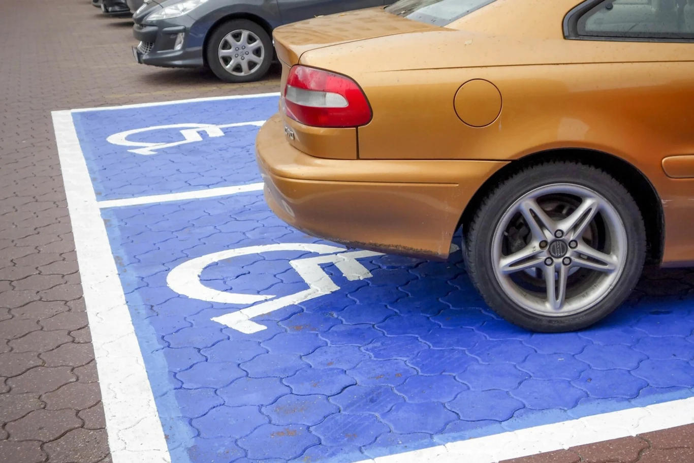 Niebieska koperta często staje się obiektem nadużyć ze strony bezczelnych kierowców. Złoty samochód osobowy zaparkowany w poprzek na dwóch miejscach przeznaczonych dla osób niepełnosprawnych, oznaczonych niebieskim tłem i białym symbolem wózka inwalidzkiego.