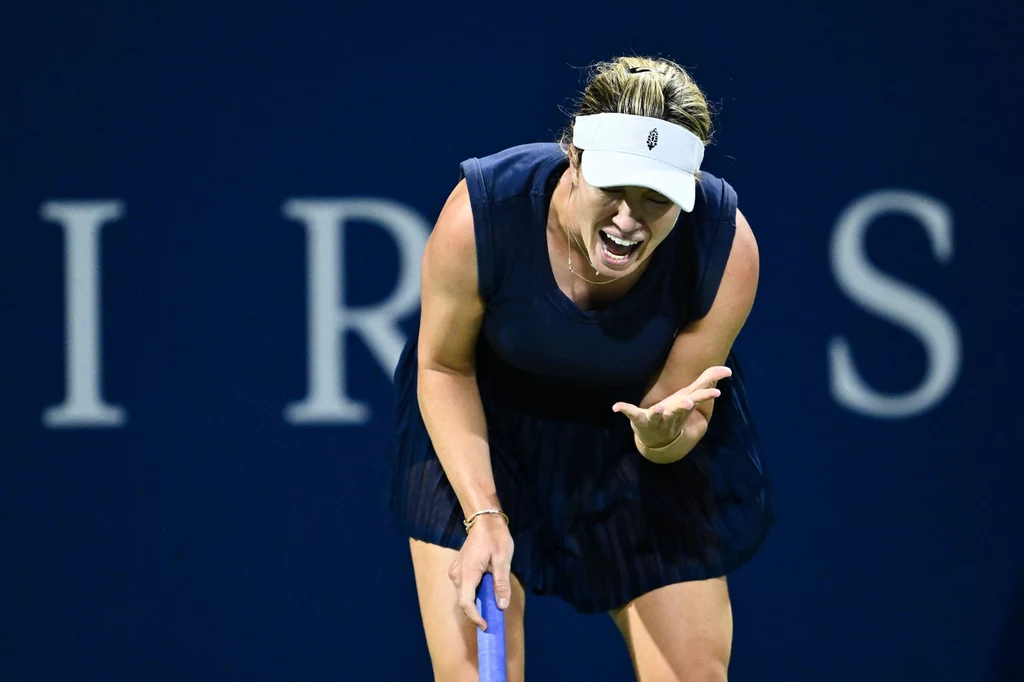 Danielle Collins Tenisistka w ciemnej sukience sportowej oraz białym daszku wyraża silne emocje podczas meczu tenisowego, pochylona do przodu, z widoczną frustracją na twarzy, na tle niebieskiego kortu.