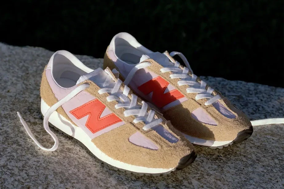 Kremowo-różowe sneakersy New Balance z pomarańczowym logo na tle kamiennej powierzchni Kremowo-różowe sneakersy New Balance z pomarańczowym logo na tle kamiennej powierzchni