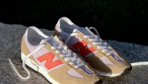 Kremowo-różowe sneakersy New Balance z pomarańczowym logo na tle kamiennej powierzchni