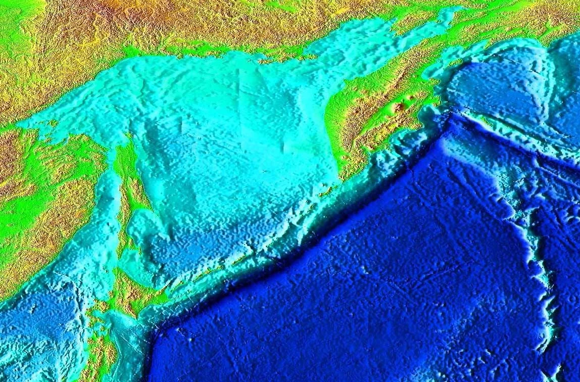 Rów Kurylsko-Kamczacki Kolorowa mapa topograficzna prezentująca ukształtowanie terenu i dna oceanicznego, z wyraźnymi różnicami wysokości i głębokości zaznaczonymi gradientami barw od zielonego, przez turkusowy po głęboki niebieski.
