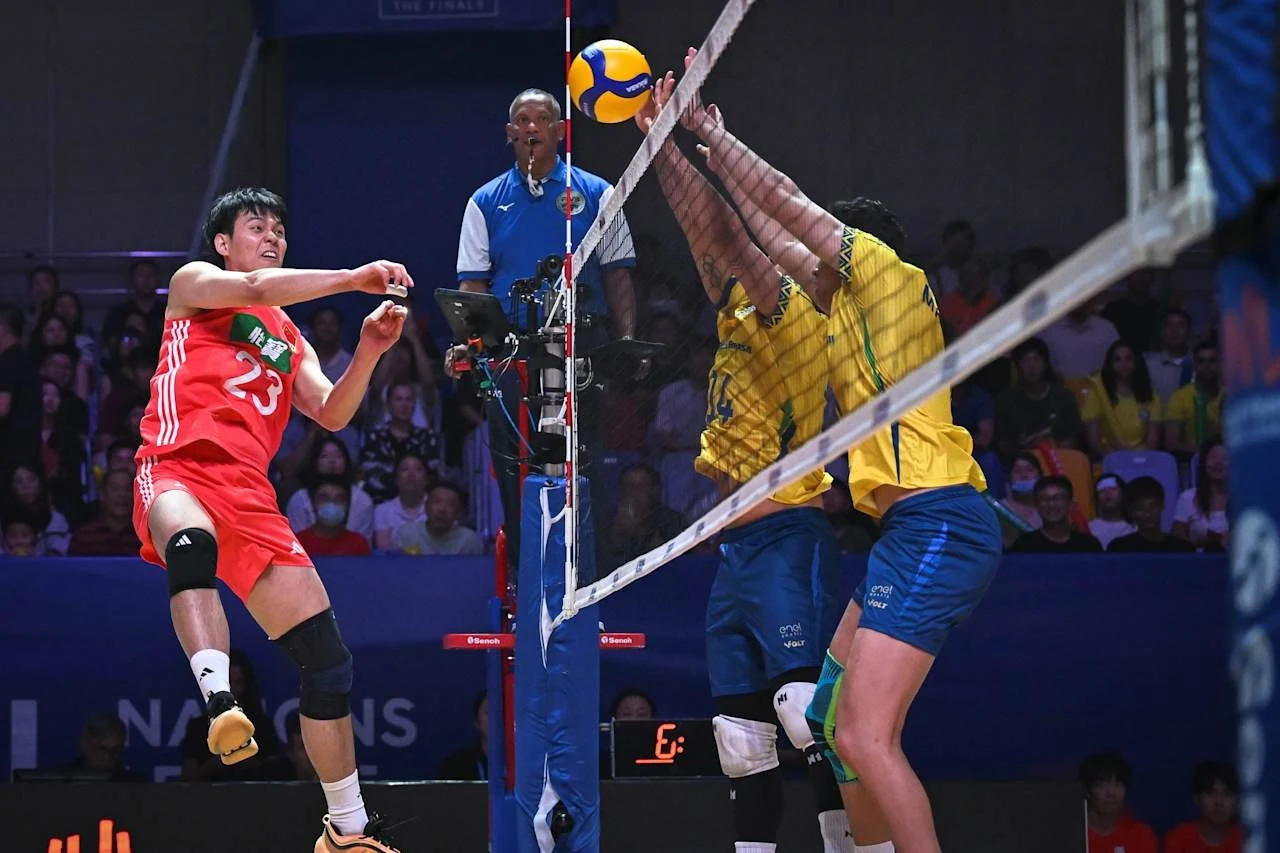Liga Narodów siatkarzy. Chińczycy zaskoczyli Brazylię w pierwszym secie Intensywna akcja podczas meczu siatkówki, zawodniczka uderza piłkę nad siatką próbując pokonać dwóch przeciwników usiłujących zablokować atak, w tle widoczny sędzia oraz publiczność.