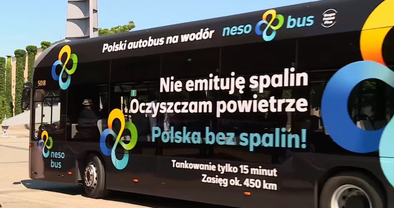 Czarny, nowoczesny autobus wodorowy z wyraźnymi napisami promującymi brak emisji spalin i oczyszczanie powietrza, na tle miejskiej przestrzeni.