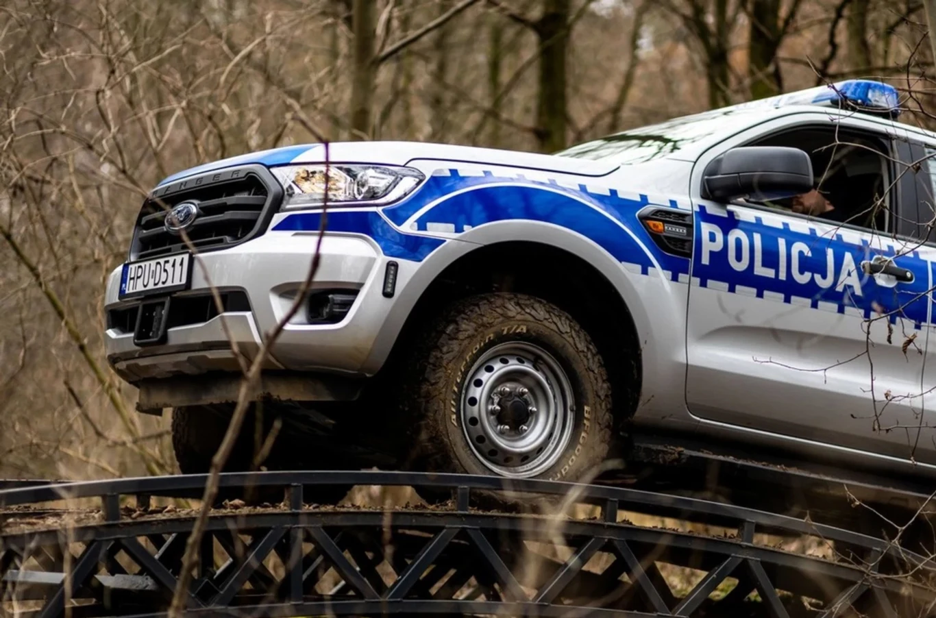 Terenowe Fordy Ranger zdobywają coraz większe powodzenie wśród służb mundurowych. Radiowóz policyjny terenowy marki Ford wjeżdżający na stalowy mostek w zalesionym terenie.