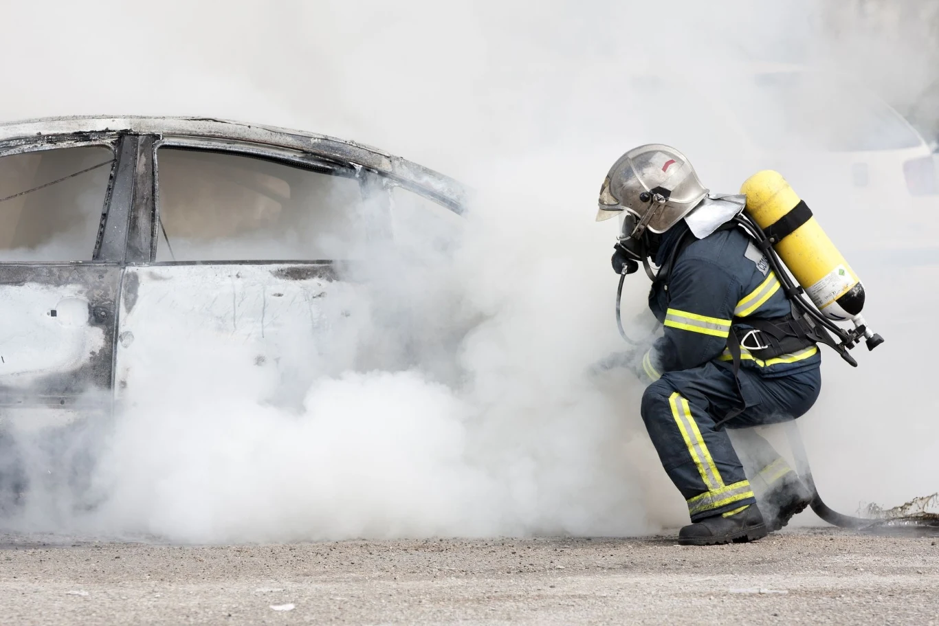 Częste pożary samochodów elektrycznych to stereotyp? Raport PNSM mówi wprost Strażak w pełnym umundurowaniu i sprzęcie ochronnym gasi płonący samochód otoczony gęstym dymem.