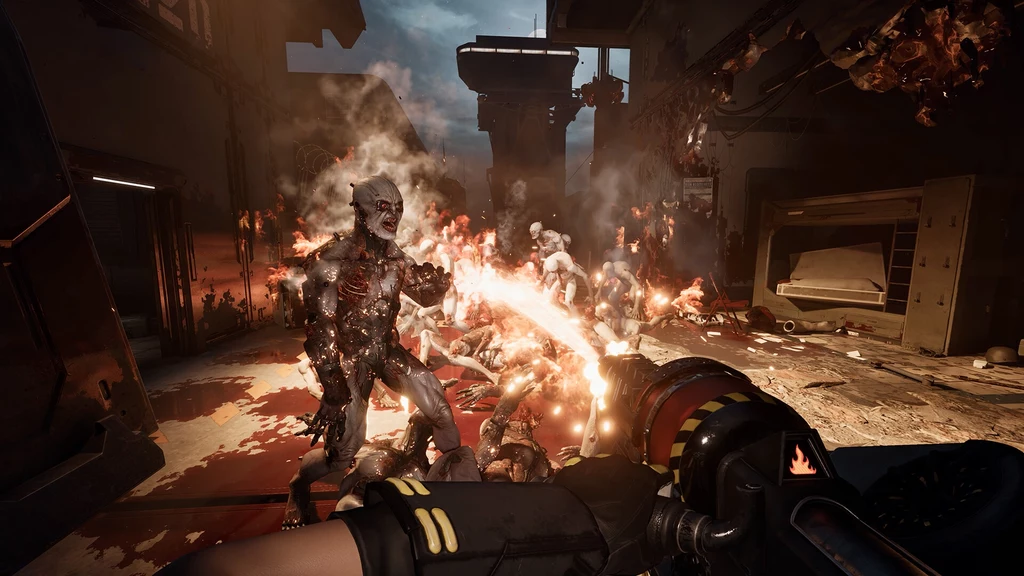 Killing Floor 3 Uzbrojona postać trzymająca miotacz ognia odpiera atak groteskowych mutantów w ciemnym, zniszczonym wnętrzu budynku; wokół widoczne są płomienie, dym i ślady zniszczeń.