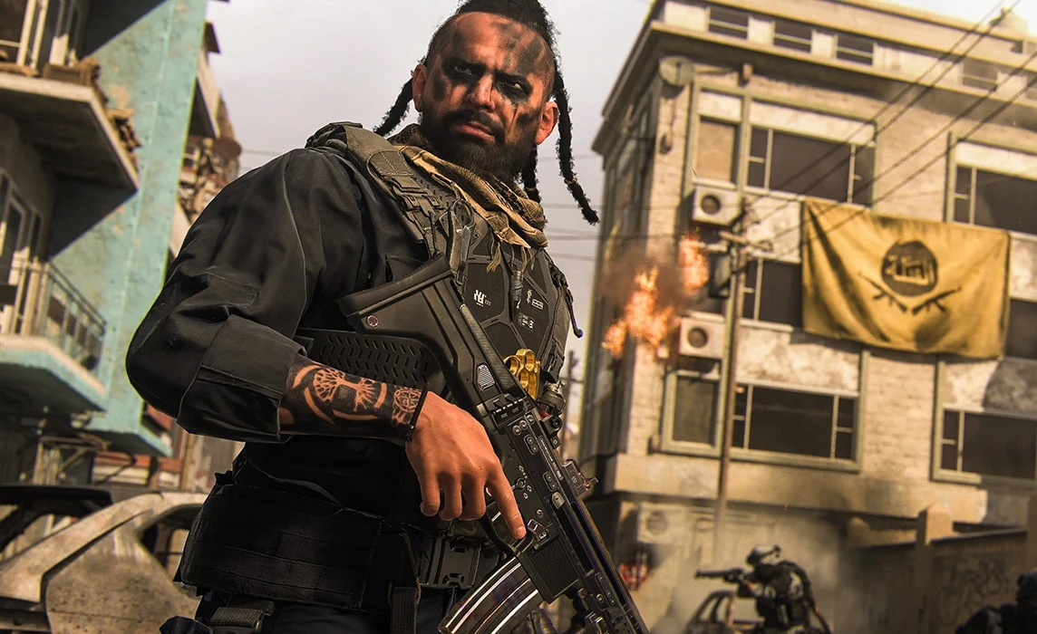 Uzbrojony mężczyzna z tatuażami i wojennym makijażem trzyma broń w rękach, stojąc na tle zniszczonych miejskich budynków, z płonącym ogniem i flagą na jednym z budynków, w otoczeniu zupełnie zniszczonego środowiska.