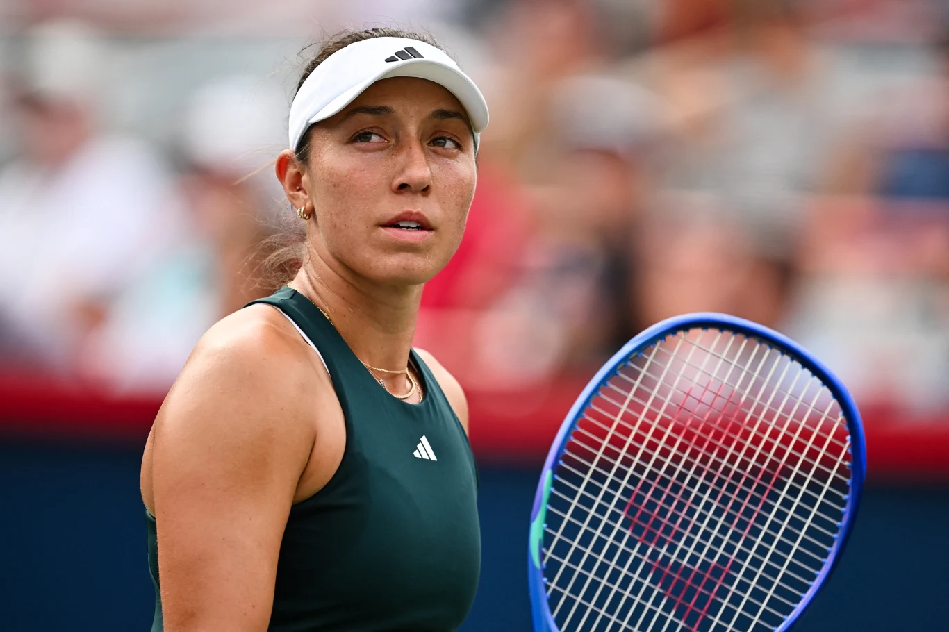 Jessica Pegula Tenisistka w ciemnozielonym stroju i białej opasce na głowie trzyma rakietę tenisową z niebieską ramą, patrzy w bok na tle rozmytych trybun.