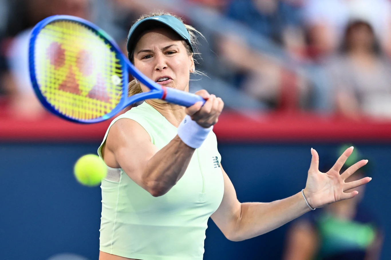 Eugenie Bouchard Tenisistka w ruchu uderzająca piłkę rakietą podczas meczu na korcie, widoczna intensywna koncentracja na twarzy zawodniczki.