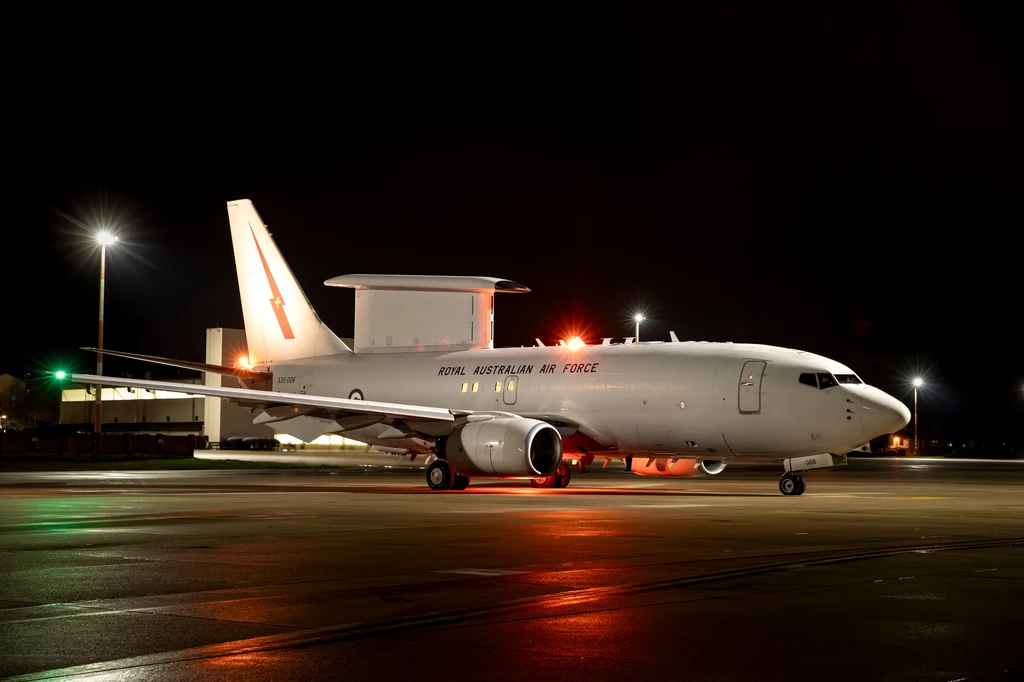 E-7A Wedgetail na lotnisku w Ramstein Duży wojskowy samolot należący do Royal Australian Air Force stoi na oświetlonym betonowym pasie startowym w nocy, wyróżnia się charakterystyczną konstrukcją radaru nad kadłubem oraz jasnym, białym malowaniem.