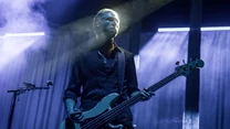Muzyk grający na gitarze basowej na scenie koncertowej, otoczony efektownym oświetleniem i dymem scenicznych reflektorów.