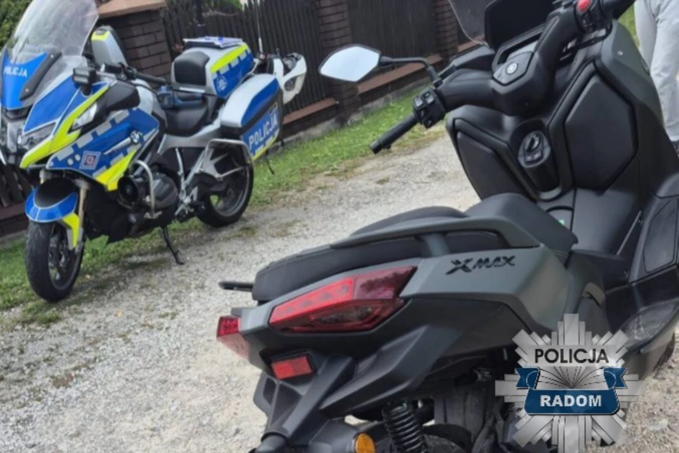 17-latek nie posiadał odpowiednich uprawnień do kierowania motocyklem. Sprawa trafiła do sądu. Policyjny motocykl z charakterystycznym niebiesko-żółtym oznakowaniem stoi zaparkowany obok czarnego skutera XMAX, w tle ogrodzenie z cegły oraz część umundurowanej osoby.