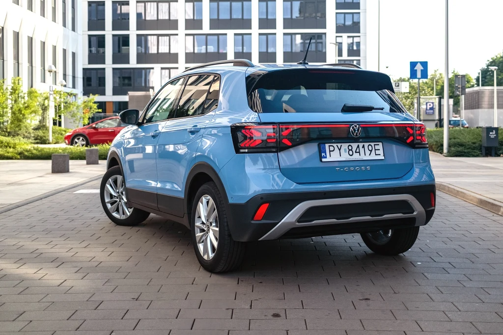 Tiguan do miasta? Volkswagen T-Cross sprawdzi się nawet w roli jedynego samochodu w rodzinie Niebieski samochód osobowy Volkswagen T-Cross zaparkowany na tle nowoczesnych budynków biurowych, w słoneczny dzień, liczne elementy infrastruktury miejskiej w tle.