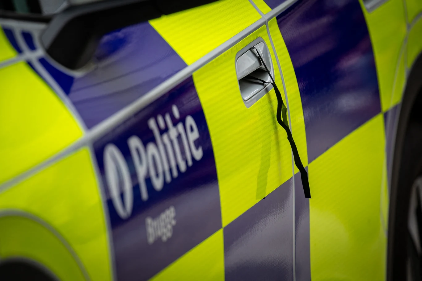 Ciało 39-letniego Polaka w opuszczonym domu w belgijskim mieście Torhout Fragment radiowozu policyjnego z napisem „Politie”, pokryty żółto-niebieską szachownicą, detal klamki z przewieszonym czarnym paskiem.