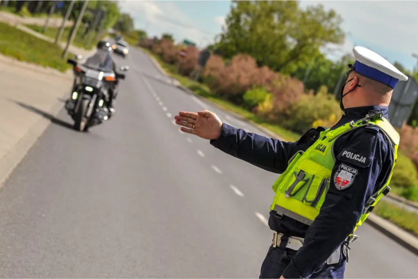 Sąd niesłusznie ukarał motocyklistę za jazdę bez odpowiednich uprawnień. Interweniował Rzecznik Praw Obywatelskich. Policjant w odblaskowej kamizelce i czapce daje sygnał do zatrzymania motocykliście na szerokiej, pustej ulicy otoczonej zielenią