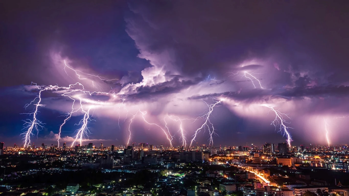 Meteorolodzy odkryli istnienie pioruna o długości aż 829 kilometrów Rozbłyski piorunów nad nocnym miastem, intensywne błyskawice rozświetlające ciemne, burzowe niebo, panorama miejskich świateł kontrastująca z naturalnym żywiołem.