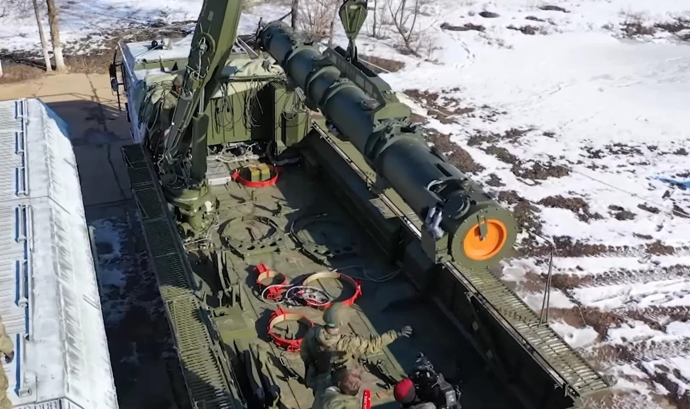 Pociski Iskander ponownie spadły na terytorium Ukrainy. Tym razem w wersji Iskander-K zdolnej do przenoszenia pocisków manewrujących Ciężki pojazd wojskowy z dużą wyrzutnią rakietową, obsługiwany przez kilku żołnierzy w mundurach, ustawiony na betonowym podłożu w pobliżu terenu pokrytego śniegiem.