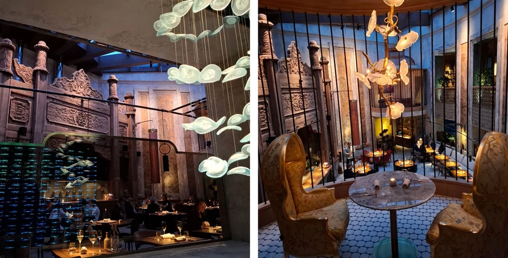 W HeJI Luksusowa restauracja z wysokimi, ozdobnymi ścianami, nastrojowym oświetleniem oraz nowoczesnymi dekoracjami sufitowymi w postaci szklanych lamp, stoły ustawione są kameralnie, w tle widoczne dekoracyjne rzeźbienia i elementy architektoniczne.