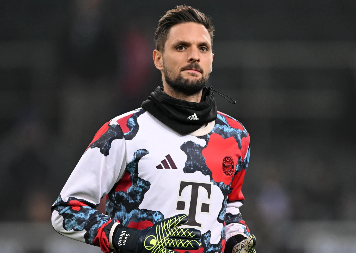 Sven Ulreich Bramkarz w kolorowej bluzie sportowej i czarnej kominiarce, w rękawicach bramkarskich, stoi na boisku, tło rozmazane.