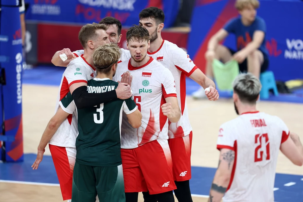 Siatkarze reprezentacji Polski Grupa siatkarzy w biało-czerwonych strojach świętuje zwycięstwo punktu na boisku, zawodnicy stoją bardzo blisko siebie, ukazując emocje i zgranie zespołowe, w tle niewyraźni kibice oraz elementy hali sportowej.