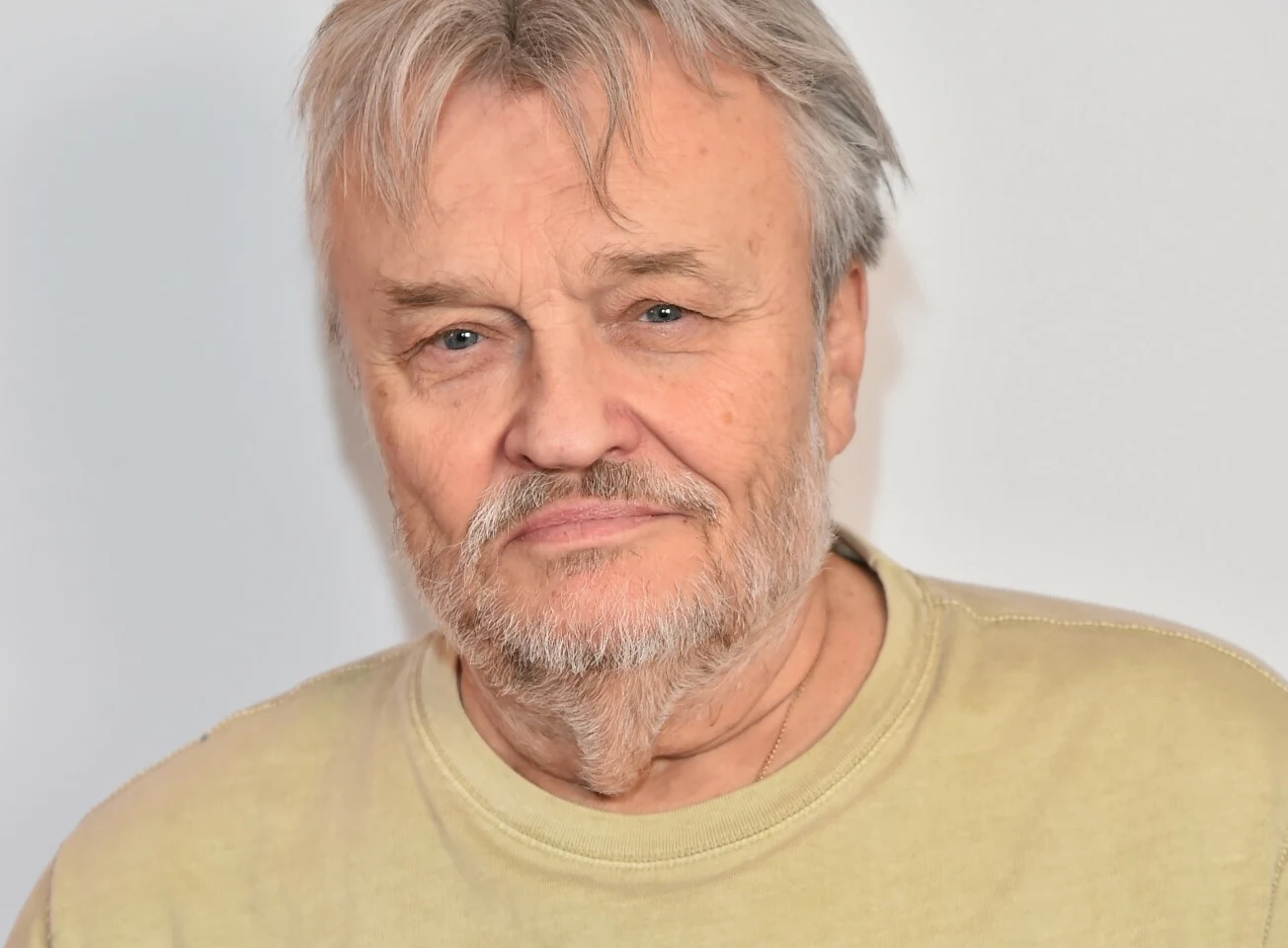 Krzysztof Cugowski pozdrowił fanów podczas wakacji Starszy mężczyzna z siwymi włosami i brodą w jasnym podkoszulku patrzący wprost do obiektywu na neutralnym tle.