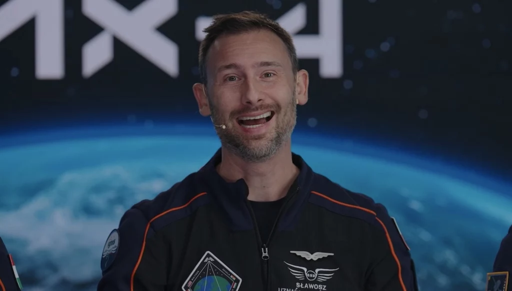 Sławosz Uznański-Wiśniewski w trakcie konferencji Axiom Space ponownie podziękował Polakom za misję Ignis. Mężczyzna w kombinezonie astronauty z naszywkami i mikrofonem na tle obrazu przedstawiającego Ziemię oraz logo SpaceX, uśmiechnięty i w trakcie wypowiedzi.