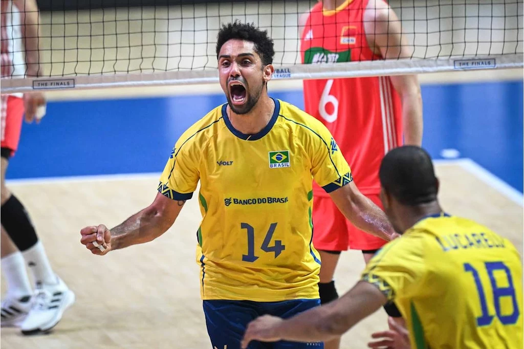 Fernando, rozgrywający reprezentacji Brazylii Zawodnik brazylijskiej drużyny siatkówki w żółtej koszulce z numerem 14 wyraża intensywne emocje w trakcie meczu, obok niego inny zawodnik z numerem 18, za siatką widoczni zawodnicy drużyny przeciwnej w czerwonych strojach.