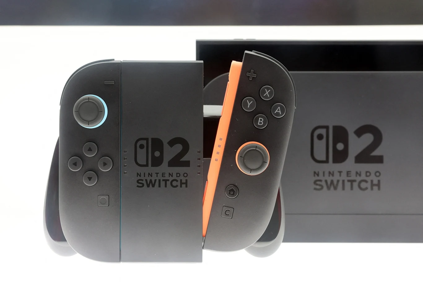 Nintendo Switch 2 Czarna konsola do gier Nintendo Switch 2 z dwoma kontrolerami Joy-Con, jeden w kolorze szarym, drugi pomarańczowy, na tle logo konsoli.