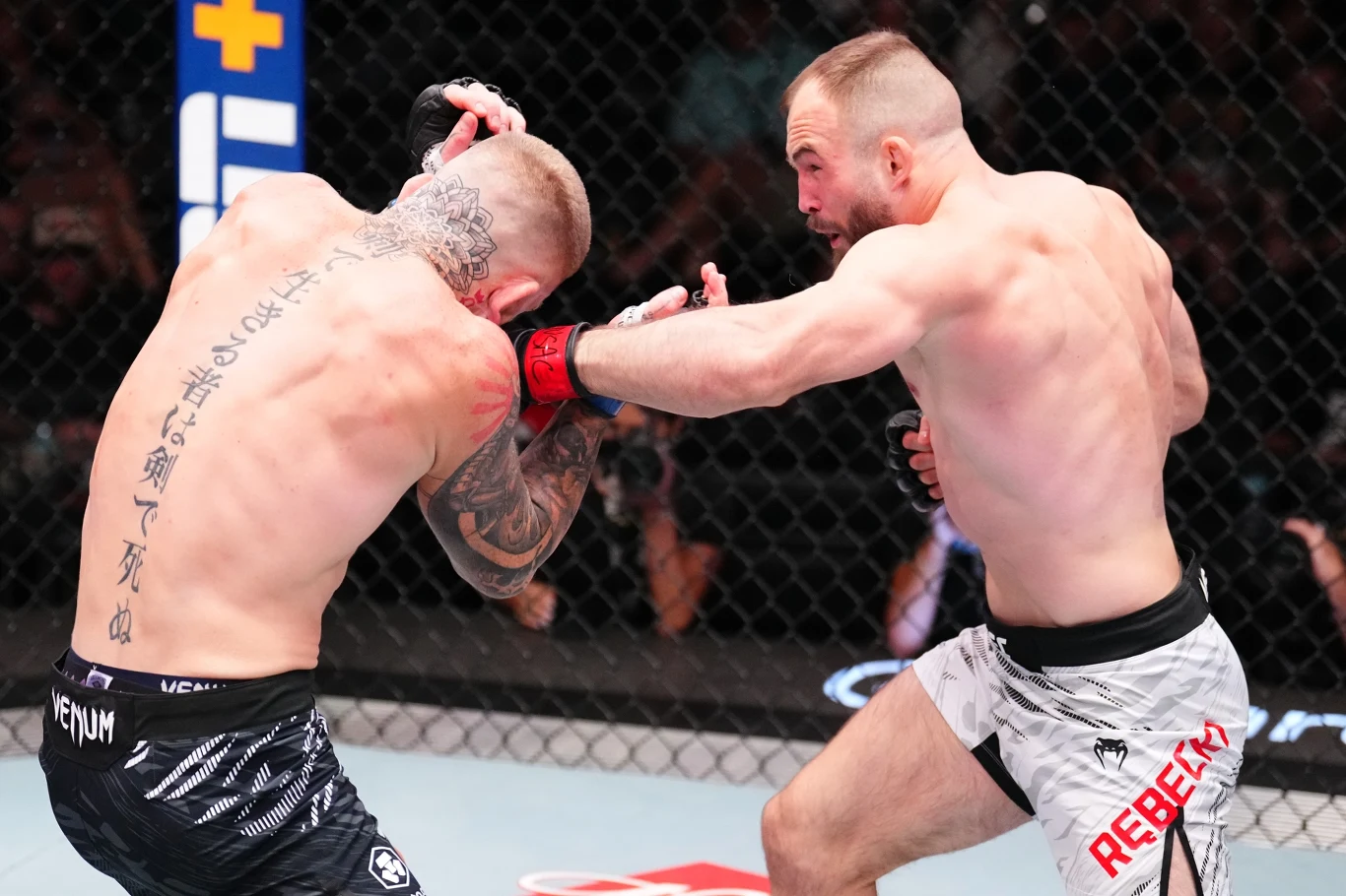 Chris Duncun - Mateusz Rębecki na UFC Vegas 108 Dwóch zawodników walczy ze sobą w klatce podczas gali MMA, jeden z nich zadaje przeciwnikowi cios w twarz, w tle widać siatkę oktagonu i rozmytą publiczność.