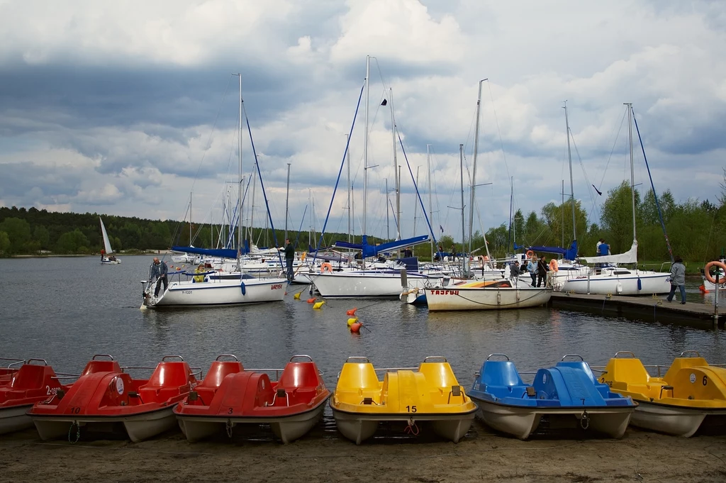 Jedną z funkcji zalewu jest turystyka i rekreacja Przystań z rzędem kolorowych rowerów wodnych ustawionych na brzegu jeziora, w tle cumujące jachty żaglowe oraz ludzie spacerujący po pomoście, wokół zieleń drzew i pochmurne niebo