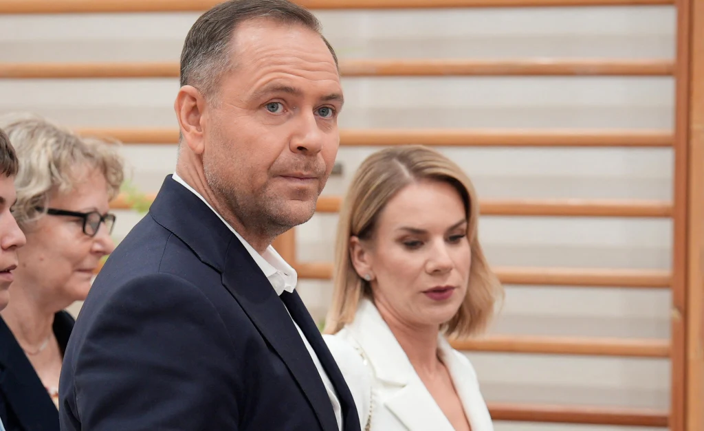 Cztery osoby w eleganckich ubraniach stoją razem w jasnym wnętrzu, w tle poziome drewniane drabinki gimnastyczne.