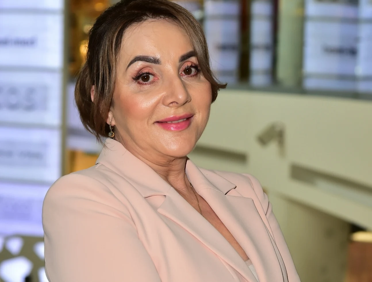 Danuta Martyniuk przeszła metamorfozę Kobieta o jasnej karnacji, uśmiechnięta, z makijażem i ciemnymi włosami upiętymi do tyłu, ubrana w jasnoróżową marynarkę, stoi w nowoczesnym, jasnym wnętrzu z rozmytym tłem.