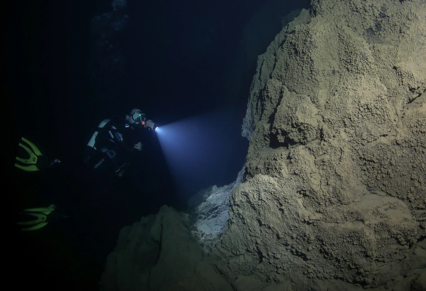 Nurkowanie w podwodnej jaskini, zdjęcie ilustracyjne Nurek z latarką podwodną eksploruje ciemną, podwodną jaskinię, oświetlając ścianę skalną pokrytą osadem.
