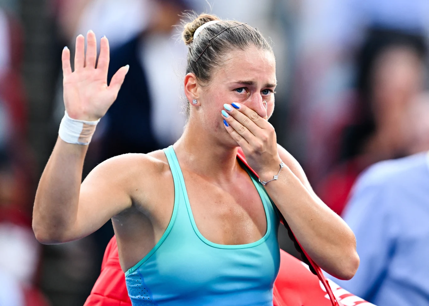 Kobieta w sportowym stroju z łzami w oczach zakrywa usta jedną ręką, a drugą unosi w geście pożegnania lub podziękowania, na twarzy widoczne silne emocje.