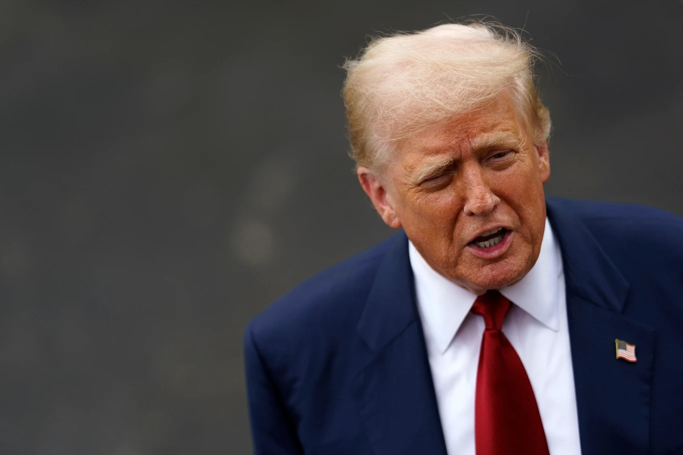 Prezydent Donald Trump Mężczyzna w garniturze z czerwonym krawatem, patrzący w bok z poważnym wyrazem twarzy na neutralnym tle.