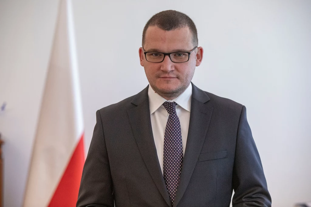 Paweł Szefernaker po wyborach został wskazany na szefa gabinetu prezydenta Mężczyzna w garniturze i okularach stoi na tle polskiej flagi, patrząc prosto w obiektyw. Ma poważny wyraz twarzy, włosy krótkie, zarost na twarzy starannie przystrzyżony.