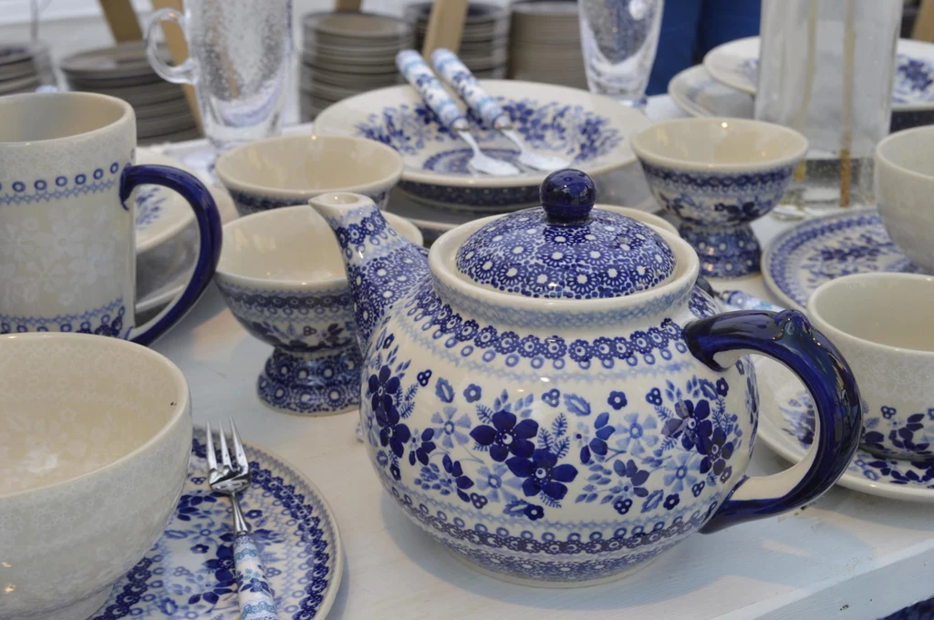 Co takiego wyjątkowego ma w sobie bolesławiecka ceramika, czego nie znajdziemy w masówce z fabryki? Bogato zdobiony porcelanowy czajnik z pokrywką i klasycznym niebieskim wzorem w kwiaty otoczony filiżankami, talerzami i innymi elementami serwisu stołowego w podobnej stylistyce.