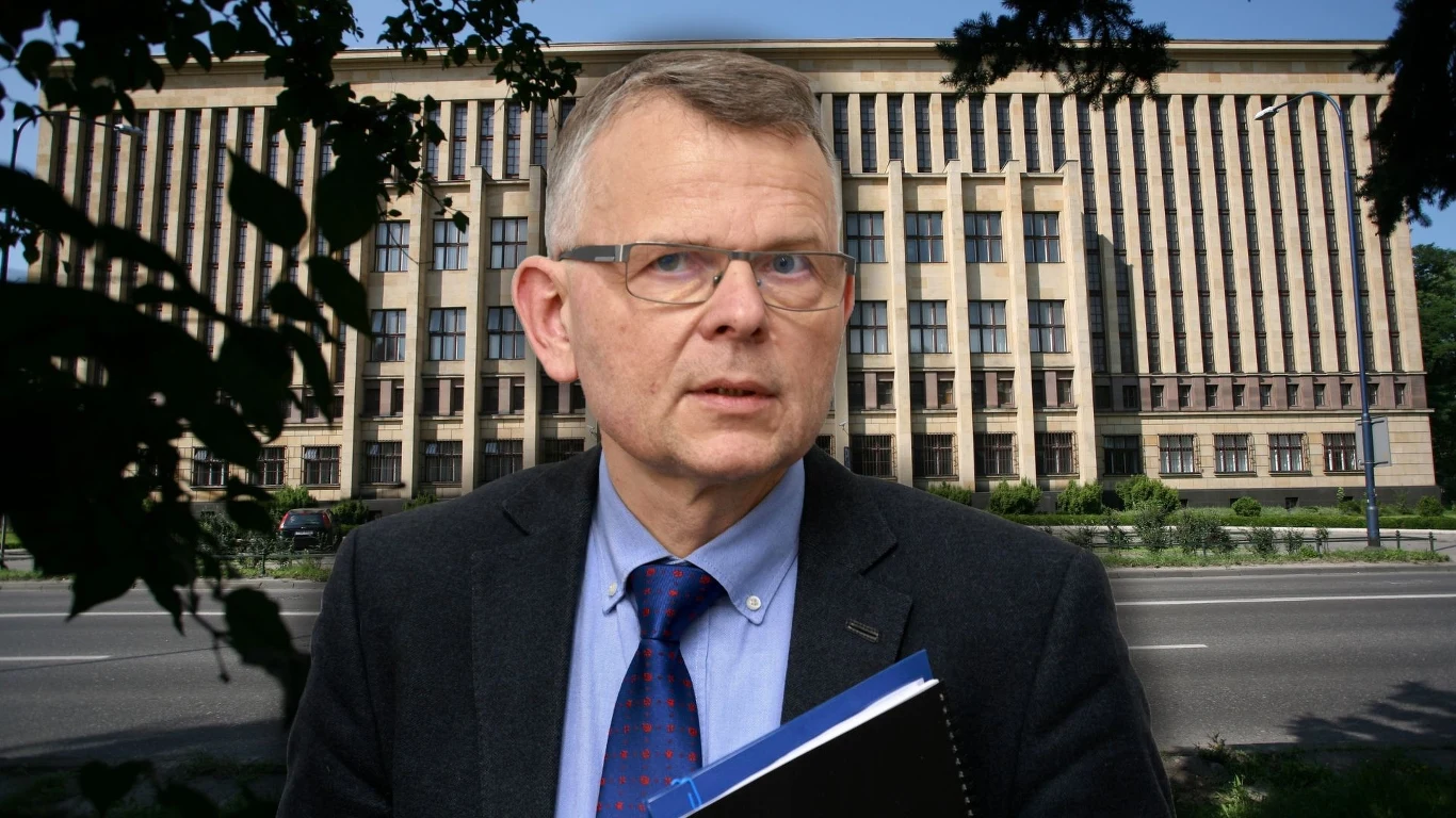 Niemiecki rząd chciałby odzyskać zabytkowe archiwa znajdujące się w Bibliotece Jagiellońskiej (na drugim planie) Mężczyzna w garniturze i okularach trzymający teczkę na tle dużego budynku użyteczności publicznej z kolumnadą i regularnie rozmieszczonymi oknami, w otoczeniu zieleni i szerokiej ulicy.