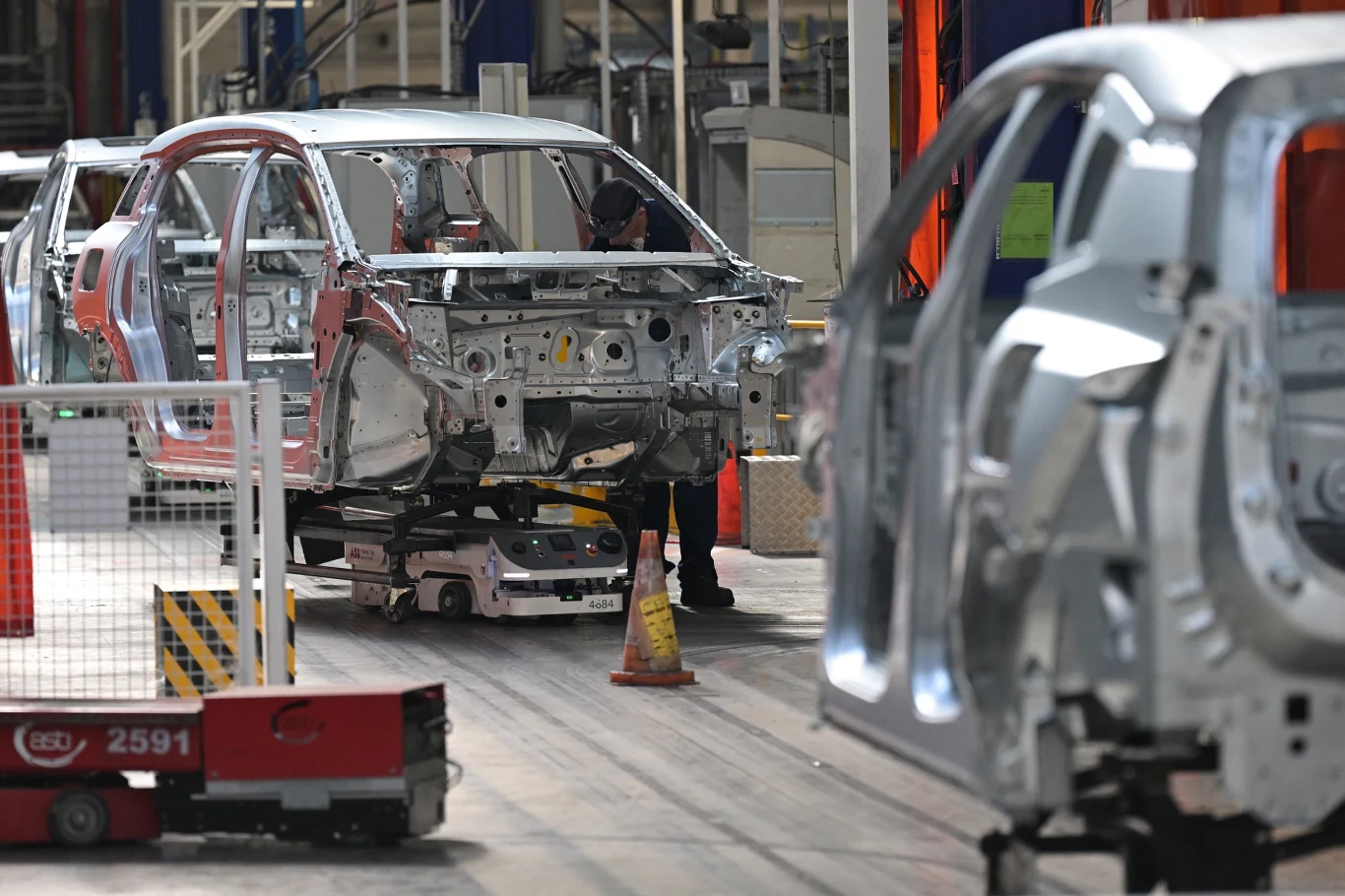 Grupowe zwolnienia, masowe bankructwa. Europejska motoryzacja w odwrocie Linia montażowa w fabryce samochodów z widocznymi szkieletowymi karoseriami pojazdów ustawionymi obok siebie oraz pracownikiem uwijającym się przy jednej z konstrukcji.