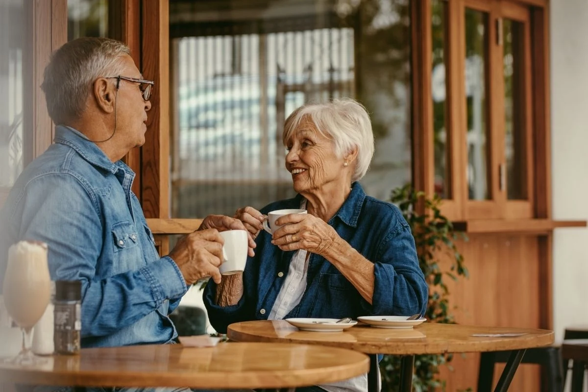 Starsza para siedzi przy stoliku w kawiarni, rozmawia ze sobą i popija kawę w spokojnej, przyjaznej atmosferze.