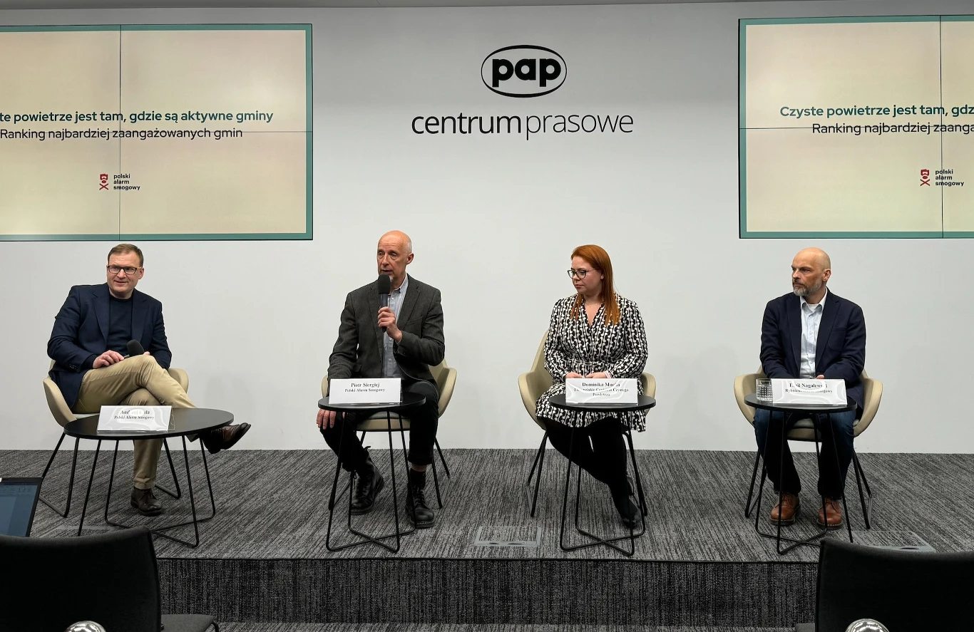 Cztery osoby siedzą na scenie w centrum prasowym PAP, przed mikrofonami i tabliczkami z nazwiskami, biorą udział w oficjalnej konferencji dotyczącej rankingu najbardziej zaangażowanych gmin w działania na rzecz czystego powietrza. Po bokach na ścianie ...