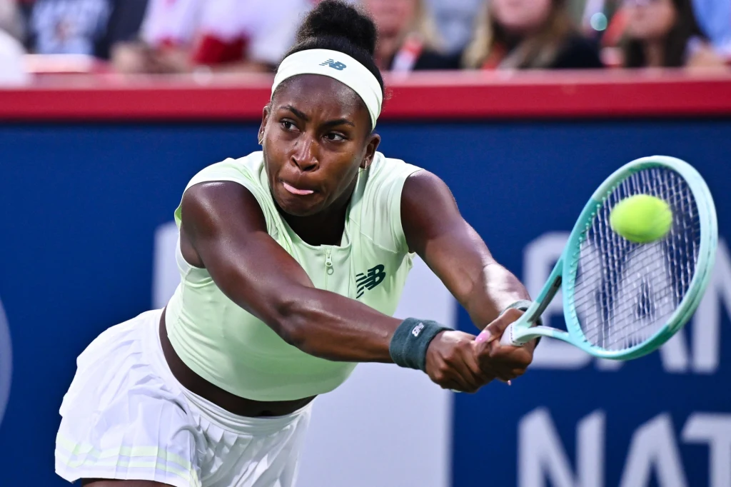 Coco Gauff Tenisistka w jasnym stroju podczas dynamicznego uderzenia piłki rakietą na korcie, skupienie na twarzy, w tle widoczna rozmyta publiczność.