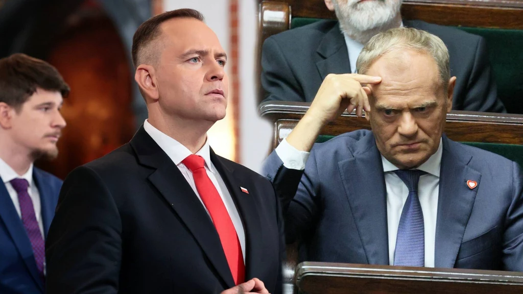 Dwóch mężczyzn w garniturach znajduje się na sali obrad, jeden stoi z poważnym wyrazem twarzy, drugi siedzi w ławie i wykonuje gest dłonią przy skroni, wyrażając skupienie lub zamyślenie. W tle widoczne są inne postacie, ubrane formalnie.