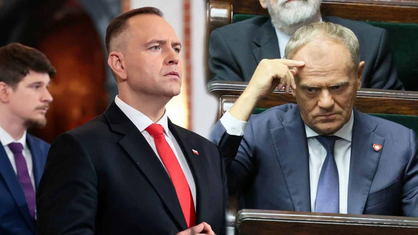 Prezydent Karol Nawrocki oraz premier Donald Tusk Dwóch mężczyzn w garniturach znajduje się na sali obrad, jeden stoi z poważnym wyrazem twarzy, drugi siedzi w ławie i wykonuje gest dłonią przy skroni, wyrażając skupienie lub zamyślenie. W tle widoczne są inne postacie, ubrane formalnie.