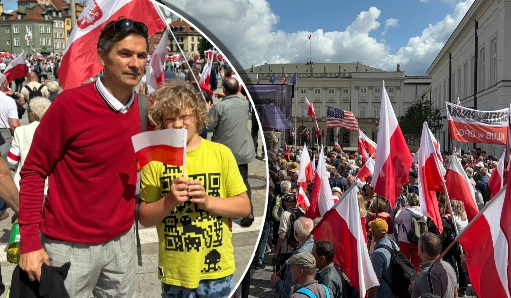 Tłum ludzi z biało-czerwonymi flagami uczestniczący w zgromadzeniu publicznym na tle miejskiej zabudowy, na pierwszym planie mężczyzna oraz dziecko trzymające flagę Polski.