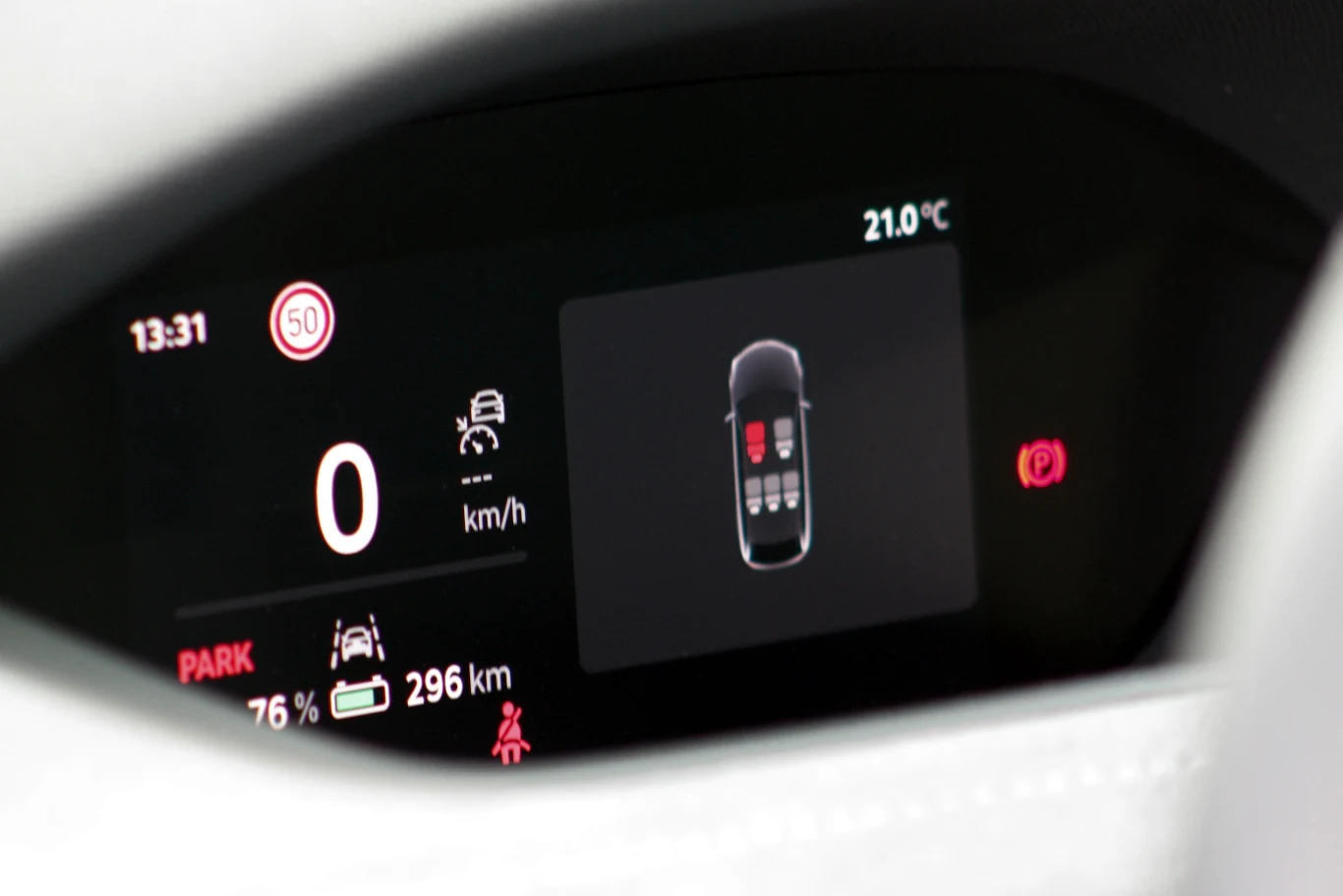 Cyfrowy wyświetlacz samochodowy z informacją o prędkości, stanie paliwa, aktualnym trybie jazdy oraz graficzną wizualizacją samochodu pokazującą otwarte drzwi. Jasny i nowoczesny panel z widoczną temperaturą zewnętrzną i poziomem naładowania akumulatora.